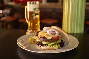 Burger mit Salat und Zwieblen auf einen weißen Teller mit einem Bierkrug